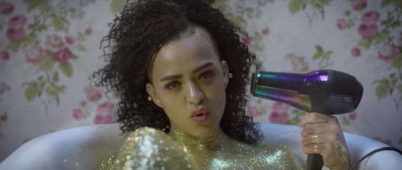 Zaena blow dries her hair while being in a gold bath 