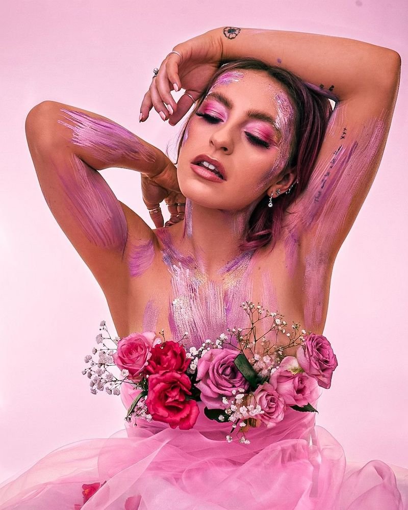 Beth McCarthy “She Gets the Flowers” press photo with face and body painted and roses decorated around her chest area