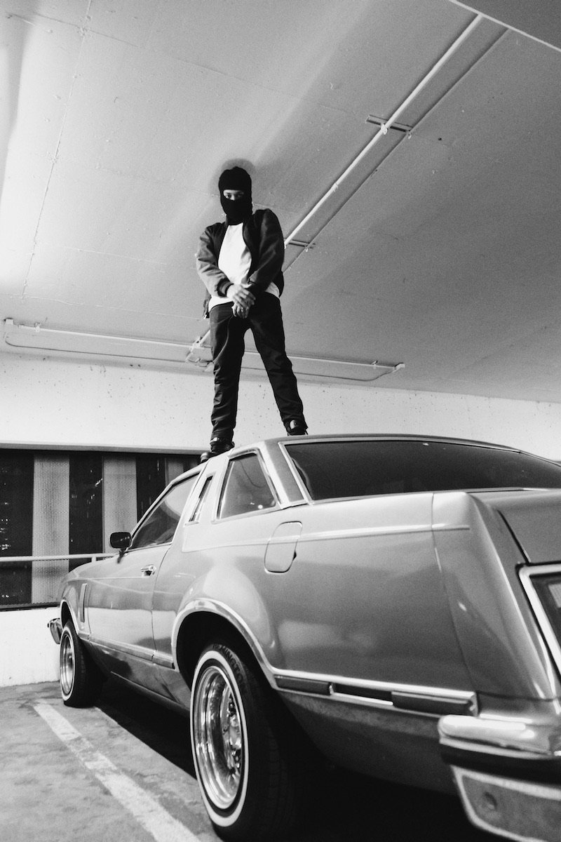 Clyde Guevara press photo standing on top of an old-school vehicle parked in a commercial garage area.