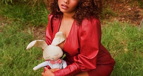Talia Jackson press outside wearing an elegant red outfit while holding a doll