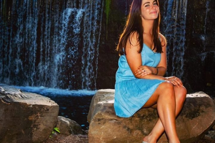 Capri Wagner press photo sitting on a rock with a waterfall in the background