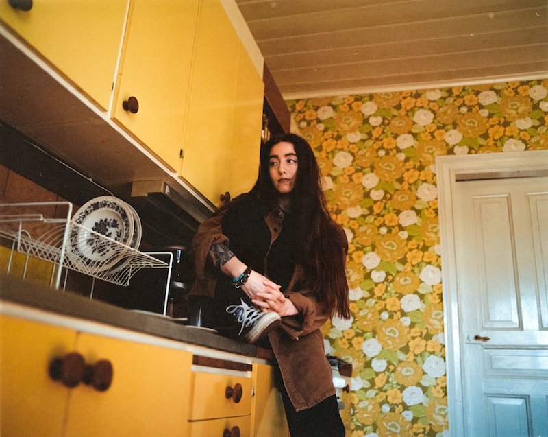 Elina - “Love Come Around” press photo inside a yellow-themed kitchen