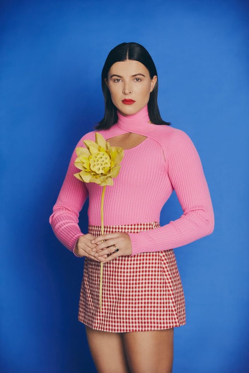 Georgia Lines press photo with a blue background holding yellow flowers 