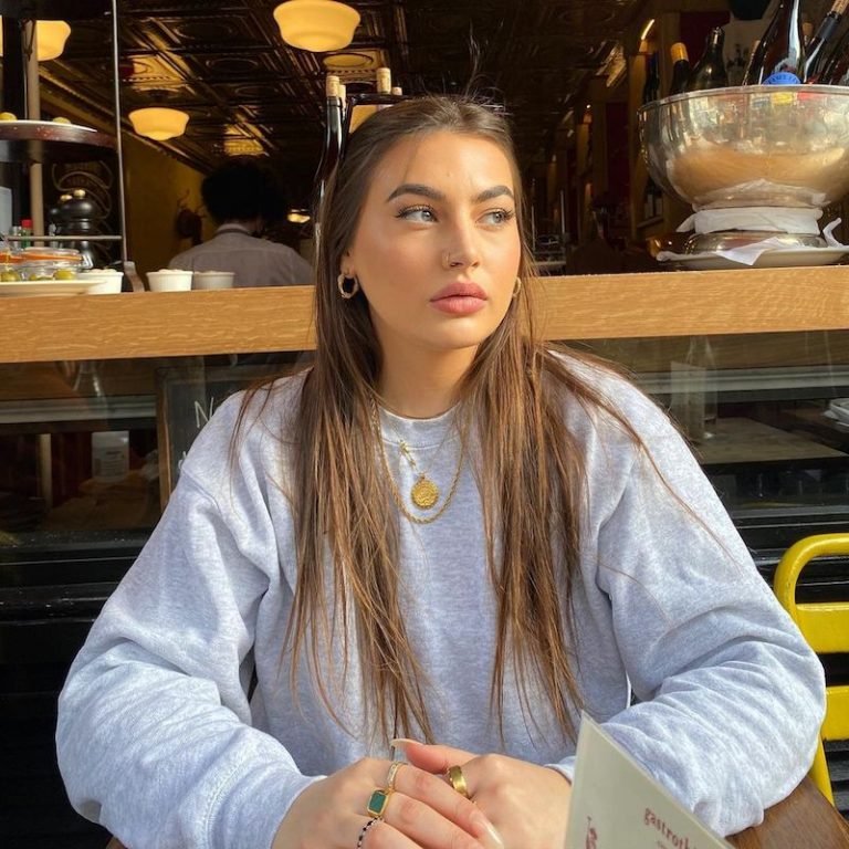 Gigi Moss press photo wearing a grey sweatshirt while seated inside an eatery
