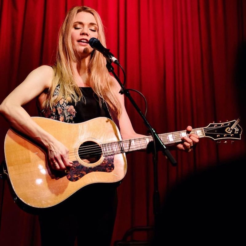 Natalie Gelman press photo singing while playing a guitar