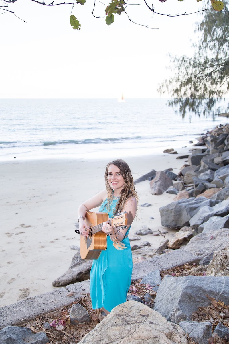 Talitha Jae press photo outside on the beach playing a guitar