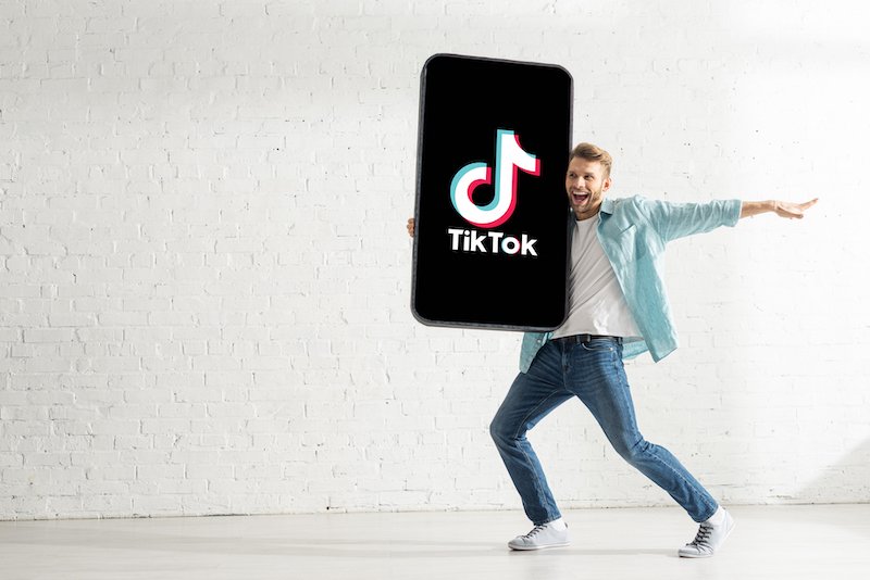 Happy man showing holding big model smartphone with TikTok app — Photo by HayDmitriy