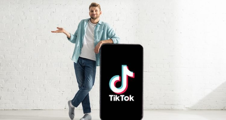 Smiling man showing confused gesture near big model smartphone with TikTok app — Photo by HayDmitriy