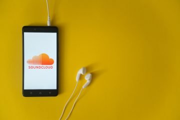 Soundcloud logo on smartphone screen and earphones plugged in on yellow background.